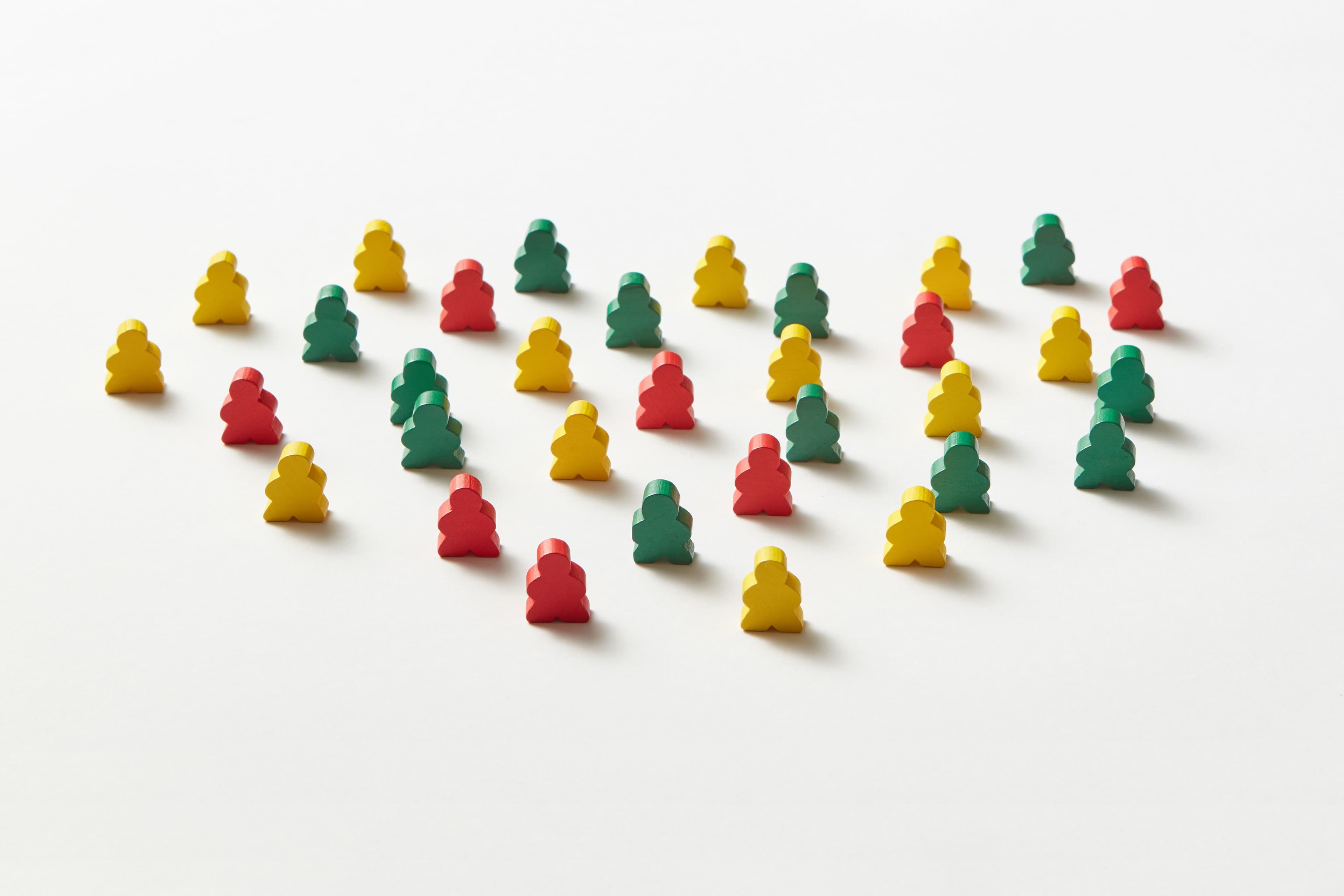 Rows of red, yellow, and green wooden meeple game pieces arranged in loose diagonal lines on a white background