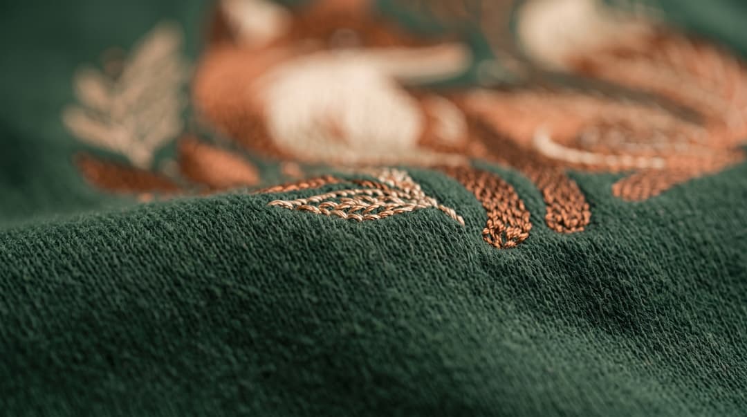 An extreme close-up of embroidered thread stitching in orange and cream forming part of a fox design on green fabric
