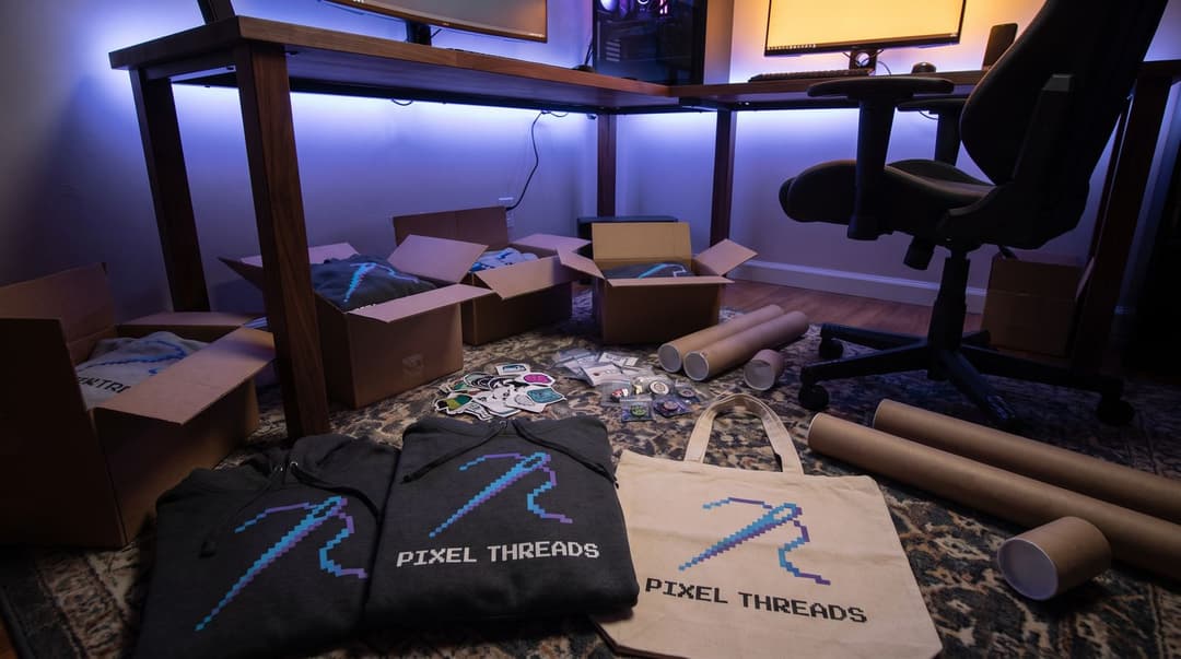 A low-angle shot of a room floor filled with open shipping boxes and piles of PIXEL THREADS branded hoodies and bags being sorted for a new merchandise launch.